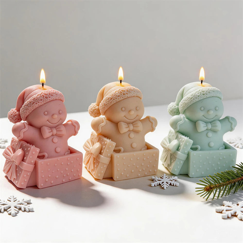 Three gingerbread gift box candles wearing winter hats in pink cream and mint