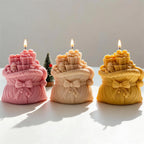 Three sculpted gift-sack candles with tiny gift boxes above their openings