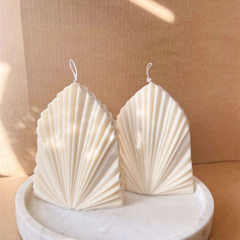 Pair of white sculptural fan-ribbed leaf candles on a round display tray