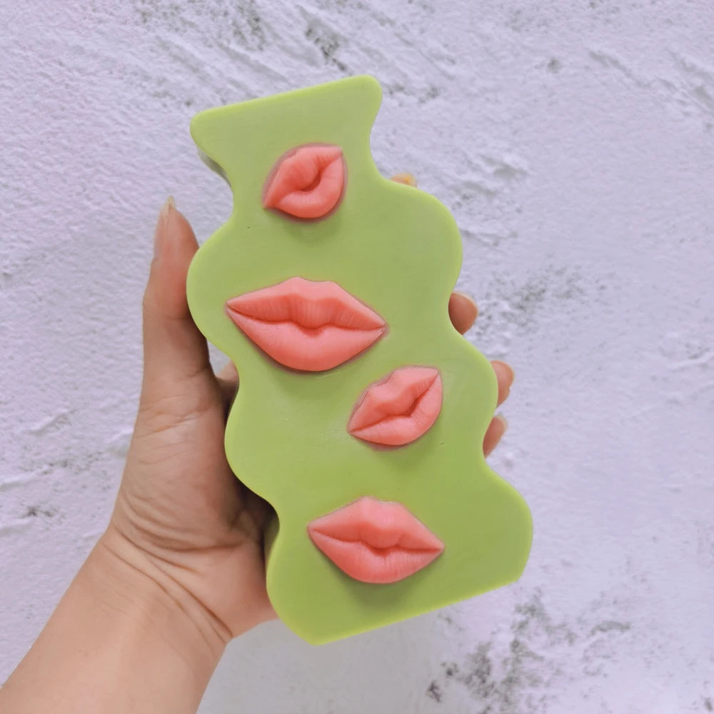 Green wavy plaque with four pink lip motifs held in one hand