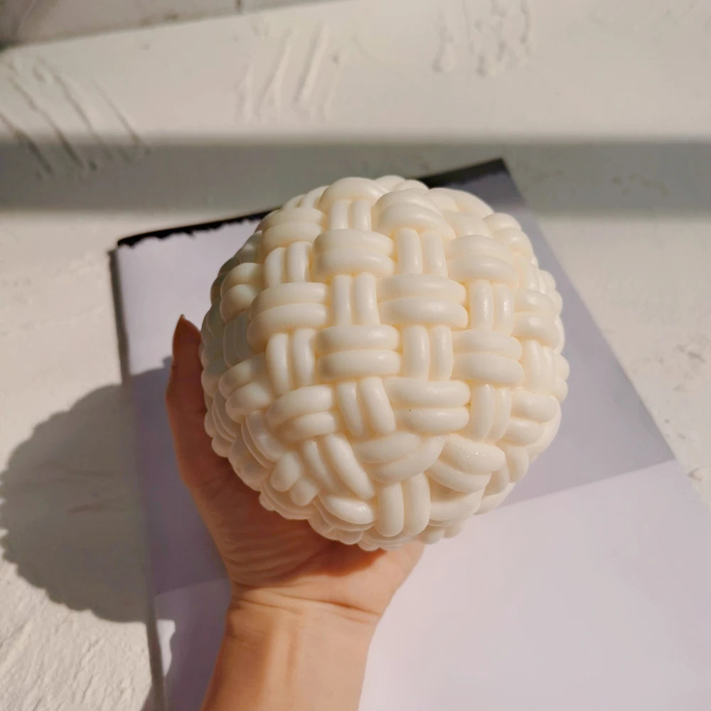 Woven ball candle held in a hand for scale