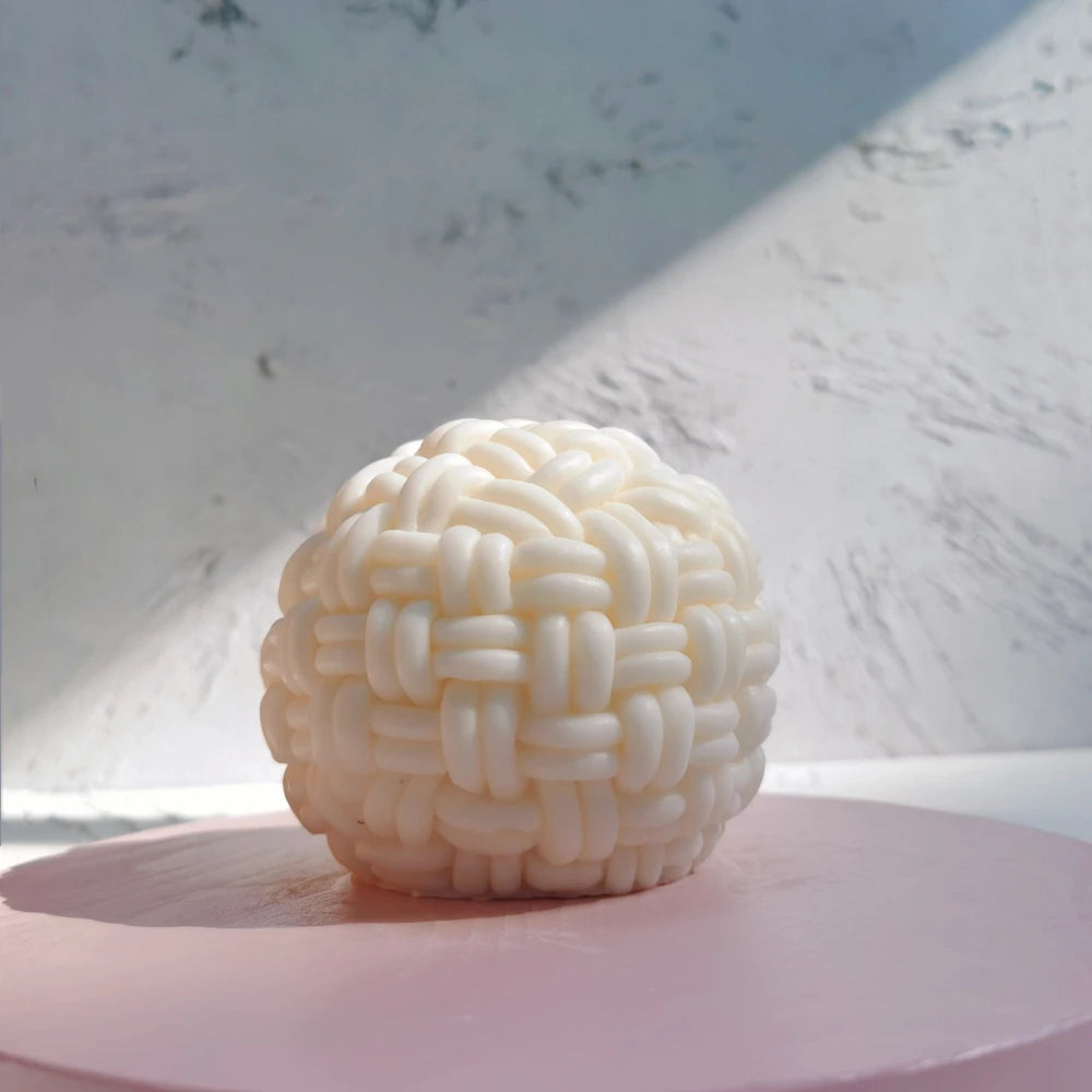 Round basket-weave candle on a pale pink platform