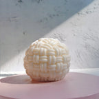 Round basket-weave candle on a pale pink platform