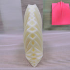 Geometric leaf candle viewed from its lattice-textured side beside the pink silicone mold