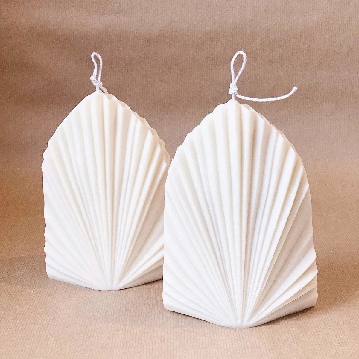Two white geometric fan-pattern candles with pointed tops
