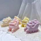 Pastel Christmas gift sleigh candles arranged on a white textile surface