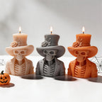 Cream, gray and orange top hat skeleton candles beside pumpkins and a decorative cobweb