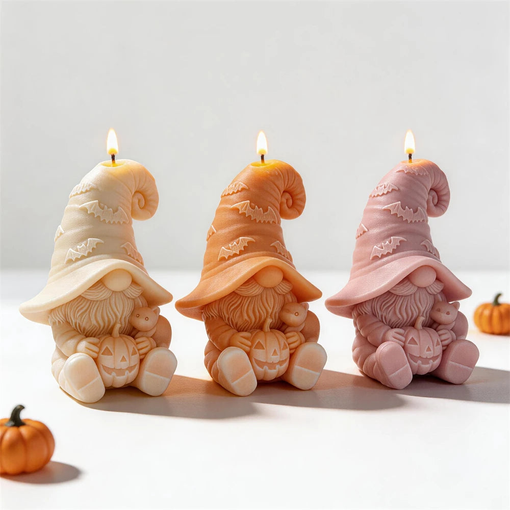 Three seated gnome candles holding pumpkins beside small cats