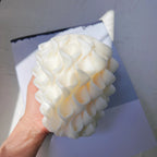Hand holding white sculptural candle showing petal texture and tapered body