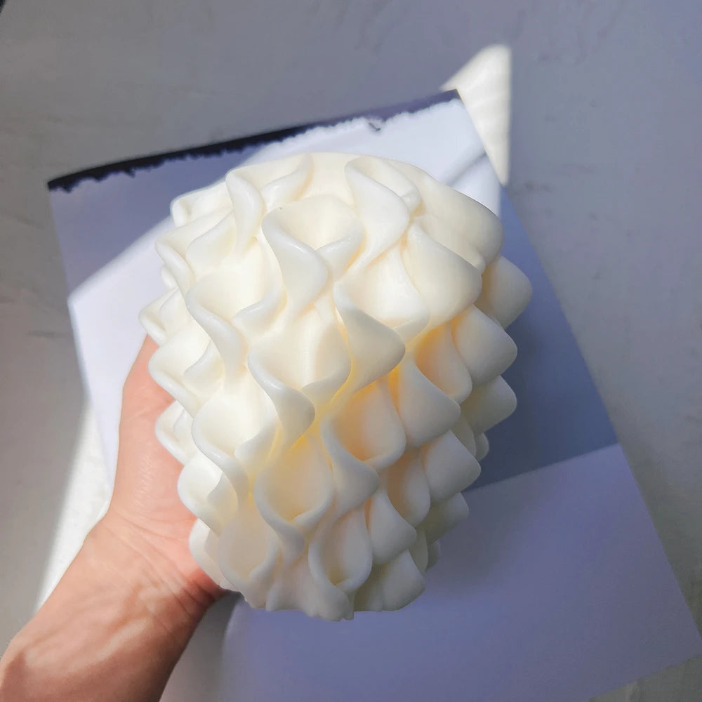 Hand holding white sculptural candle showing petal texture and tapered body