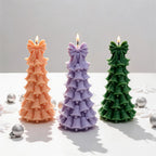 Three layered bell tree candles arranged beside festive ornaments
