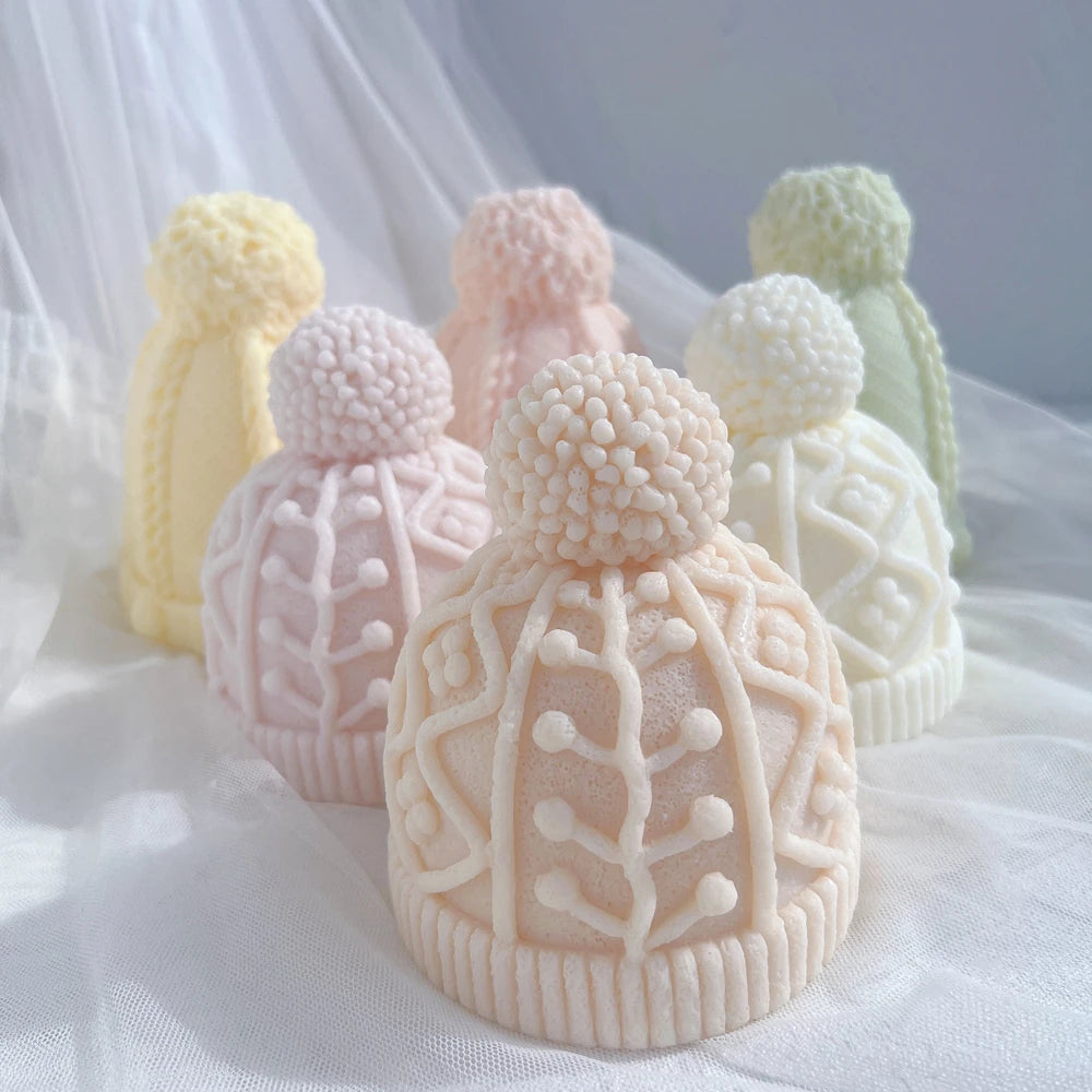Geometric knit hat candle in front of taller cable-knit hat samples