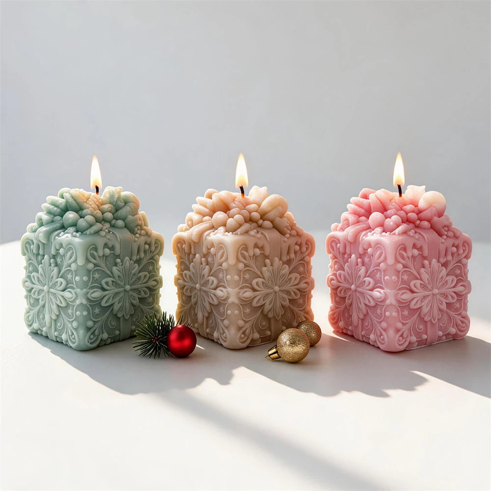 Three lit gift-box candles with ornate snowflake side relief