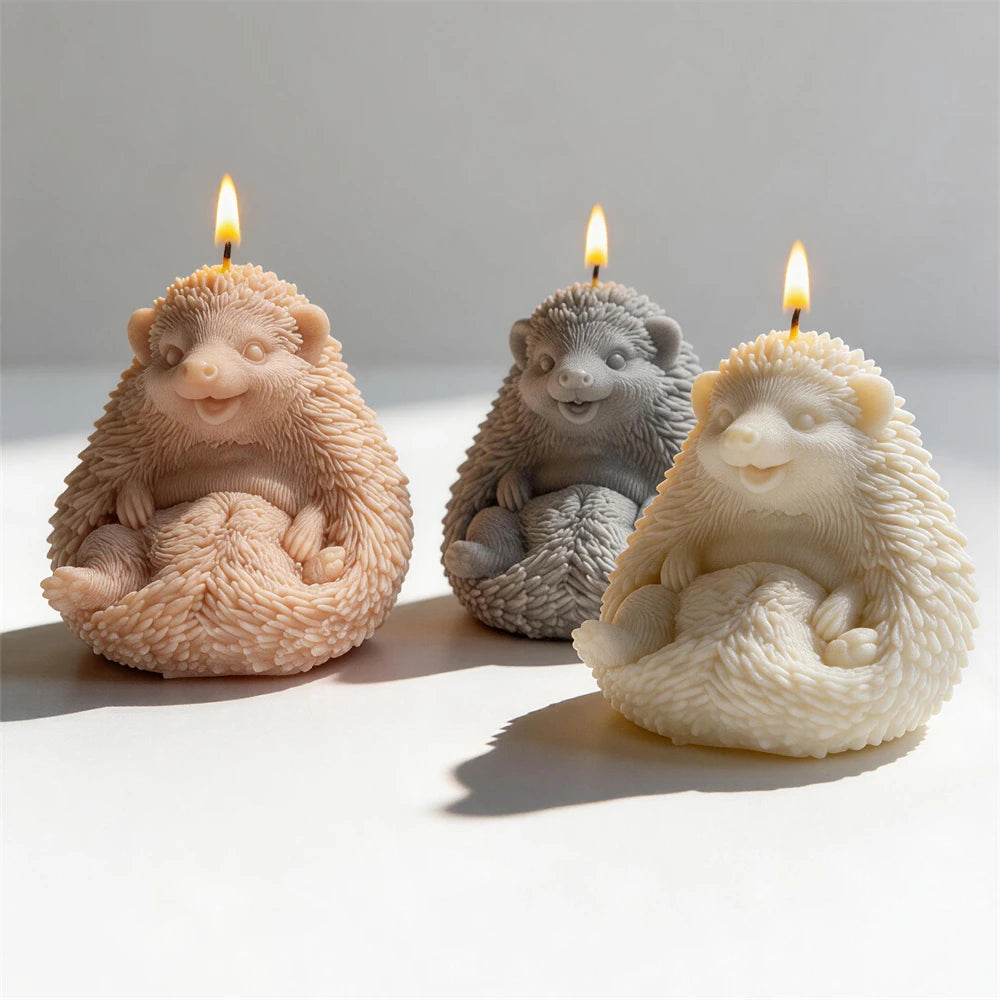 Three seated hedgehog candles in tan gray and cream with small flames