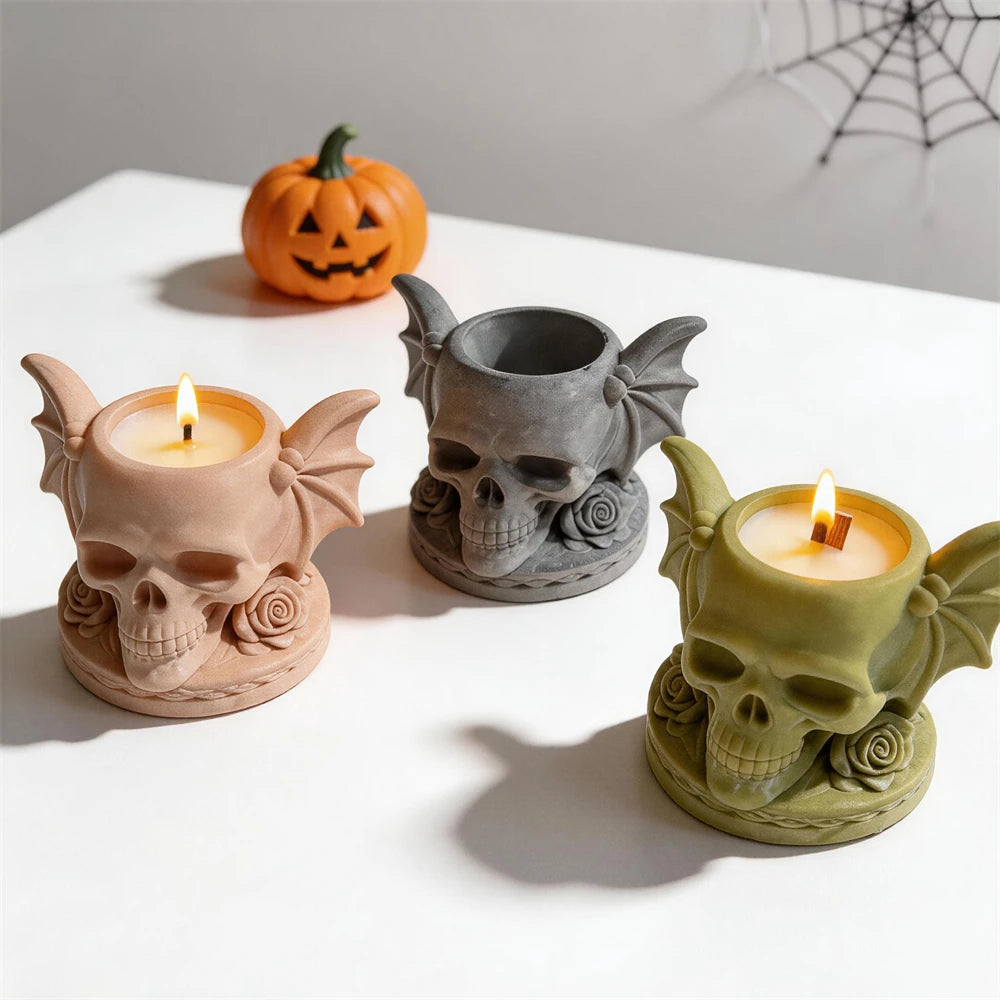Open black skull holder beside cream and green holders with lit candles