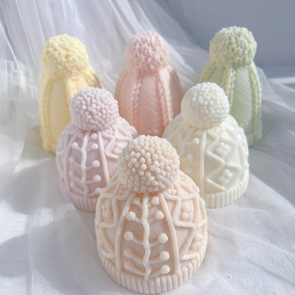 Two knit hat candle designs in pastel colors with rounded pom-poms