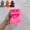Pink silicone skeleton bust mold held in a hand beside finished top hat candle samples
