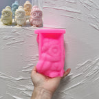 Pink silicone winter owl mold held in a hand beside hat-and-scarf candle samples