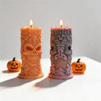 Two ornate skull pillar candles with floral scrollwork
